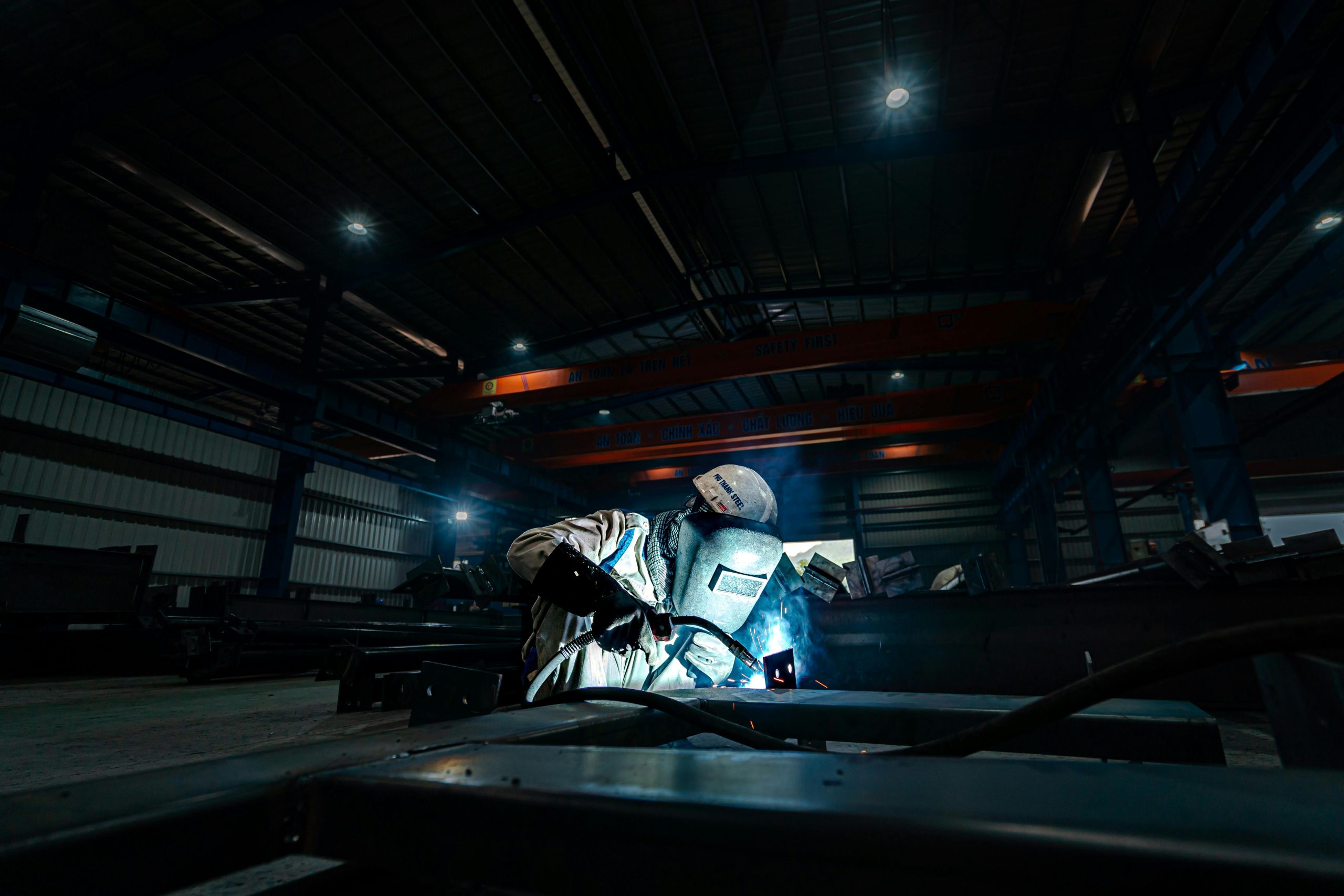 A welder working on steel structures in a large industrial warehouse, emitting bright sparks.